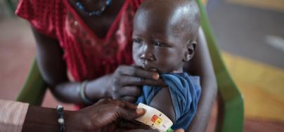 George (prénom modifié) sur les genoux de sa mère pendant que le personnel sanitaire évalue son état nutritionnel, au Soudan du Sud.