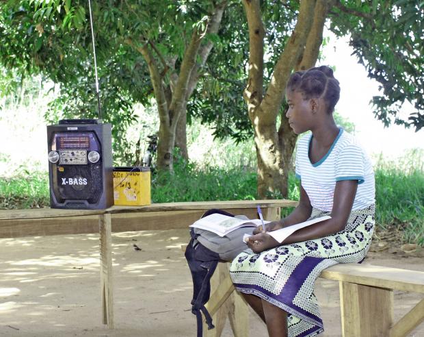  Benedita Matias listens to the voice streaming from the radio she has placed in the shade in front of her, outside the family's house near the town of Mocuba in Mozambique.