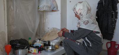 Samira, 15, a displaced girl from Aleppo by the earthquake, makes a meal of boiled potatoes and bread. Photo Credit: Dania Kareh/ Oxfam. Nehal, 47, a displaced woman from Aleppo, holds a flashlight she uses to light the way in the corridors of the shelter where she stays with her