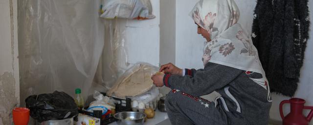 Samira, 15, a displaced girl from Aleppo by the earthquake, makes a meal of boiled potatoes and bread. Photo Credit: Dania Kareh/ Oxfam. Nehal, 47, a displaced woman from Aleppo, holds a flashlight she uses to light the way in the corridors of the shelter where she stays with her