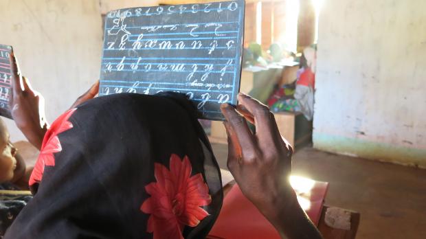 Fatima* writes the letter “e” on a small blackboard, during a literacy lesson at the headquarters of Bria’s Women Leaders Association, CAR. Credit: Godet, Oxfam