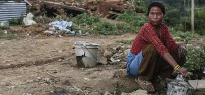 Accroupie, une femme collecte de l'eau avec un bidon en métal, dans un village de Katmandou au Népal.