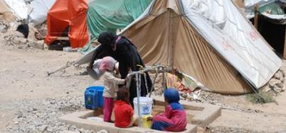 Une femme et des enfants prennent de l’eau potable à la rampe de distribution installée par Oxfam dans un camp pour personnes déplacées, à Huth. Photo : Kate Wiggans/Oxfam