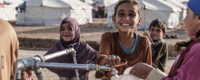 Children fill bottled with clean water at a tap stand in Hassansham camp in east of Mosul, Iraq. Credit: Tegid Cartwright/Oxfam