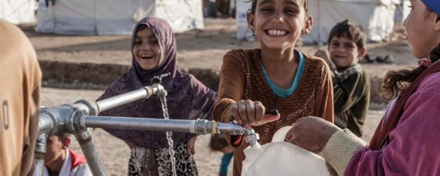 Niños llenan botellas de agua limpia en un puesto de agua en el campamento de Hassansham, Iraq. Crédito: Tegid Cartwright / Oxfam