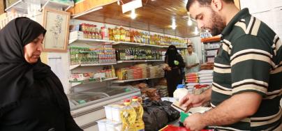 Mnwar hands the ‘Sahtein’ electronic food voucher to a shop owner to purchase food items for her family. 