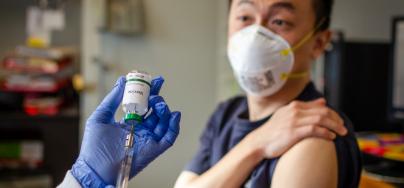 Injection being prepared by a care giver as the recipient roles up his sleeve